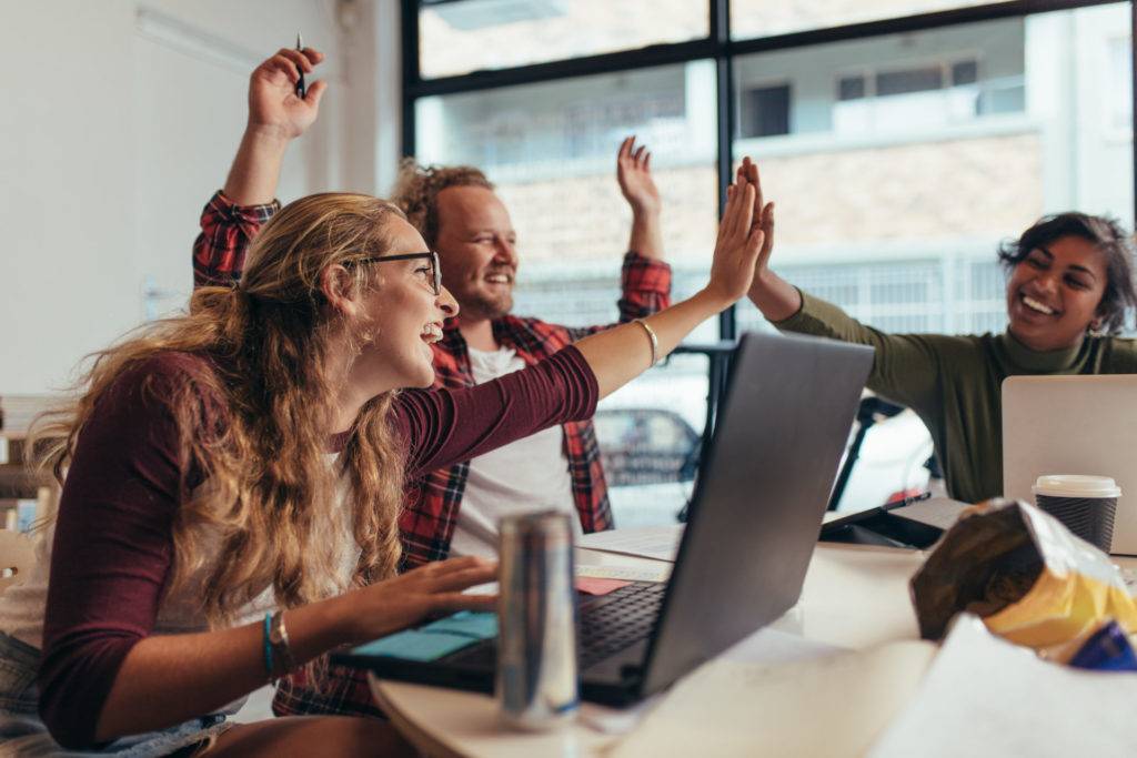 Group of young business team giving high five and celebrating success at office.